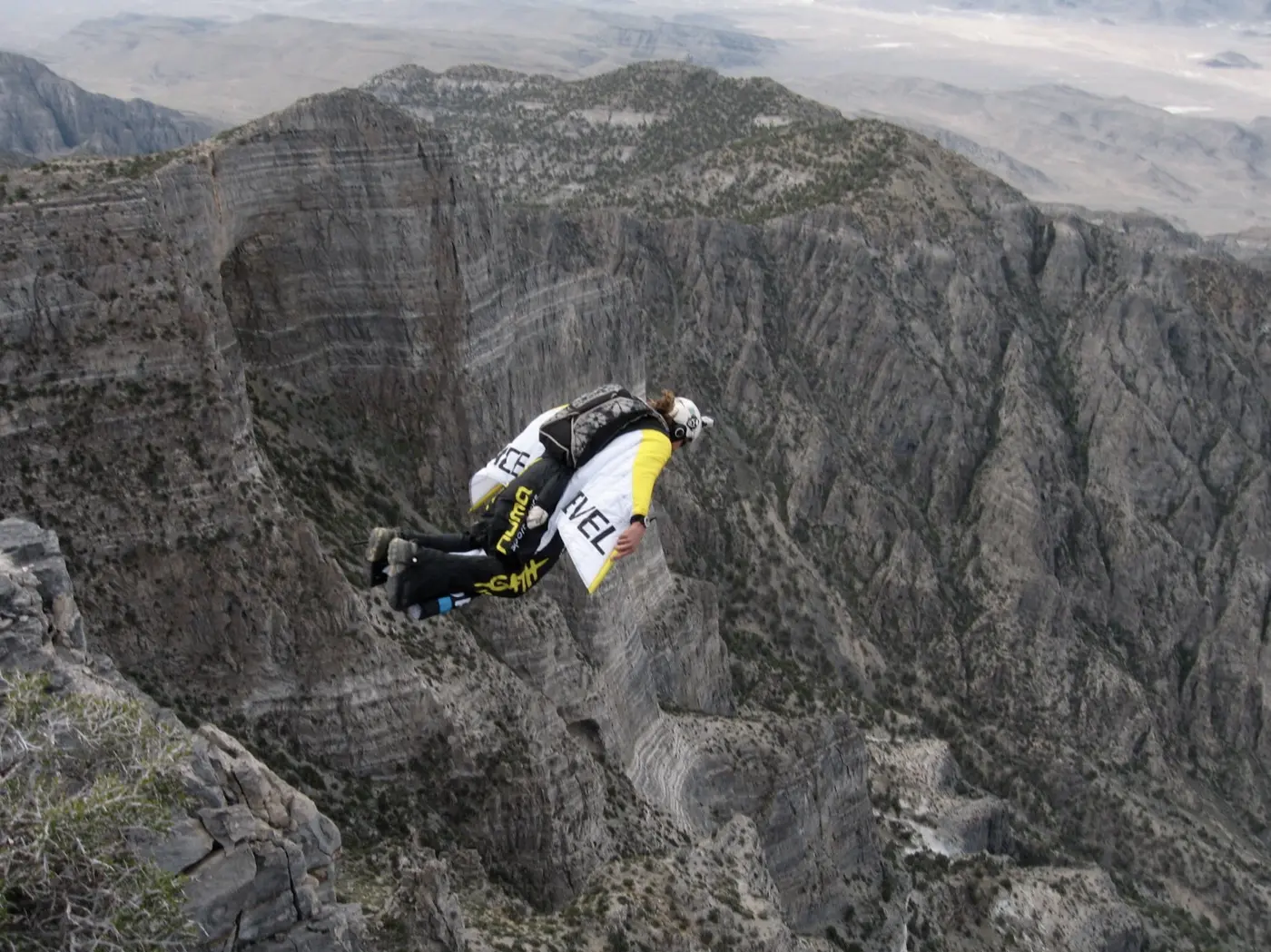 A wingsuit pilot banking past a mountain ridge