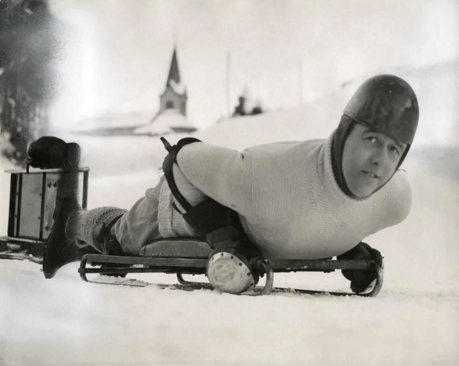 A rider in a leather helmet lying headfirst on a skeleton sled, chin up, on the Cresta Run in St. Moritz, 1935