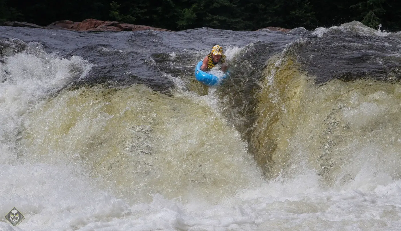 A riverboarder on a blue board dropping over a wide brown waterfall
