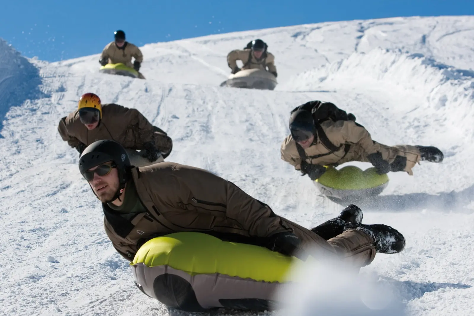 Four riders headfirst on inflatable airboards racing down a snow slope