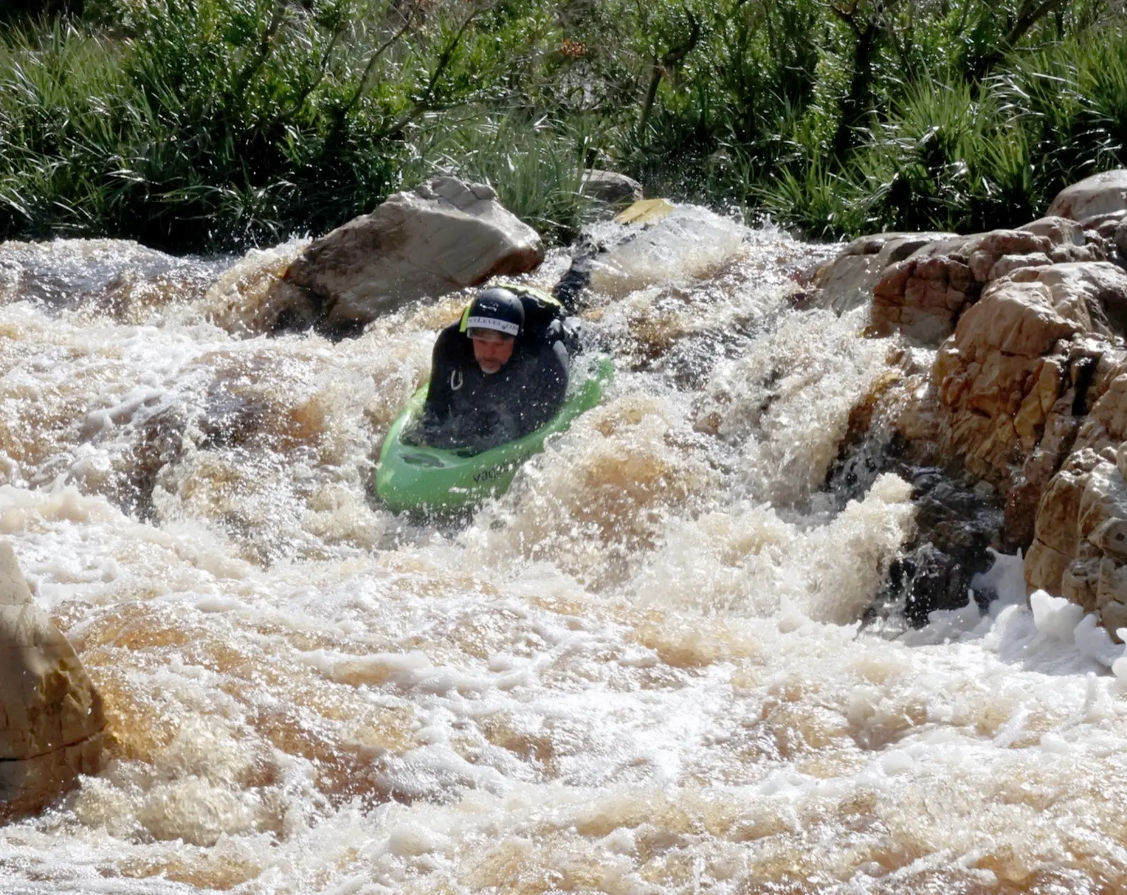 The green LEKKER Tana riverboard punching through a brown rapid on a test session