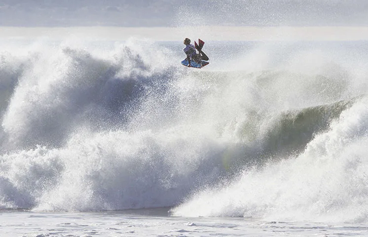 A bodyboarder launching off the lip of a huge breaking wave